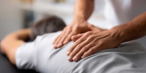 A person applying an ice pack to their lower back while seated on a comfortable sofa.