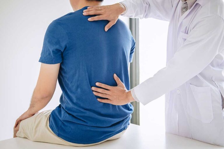 A chiropractor gently examining an older adult's back in a bright, comfortable clinic setting.